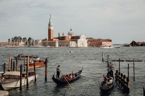 Free People floating on boats on rippling water against aged buildings with tower and dome in Venice during trip to Italy Stock Photo