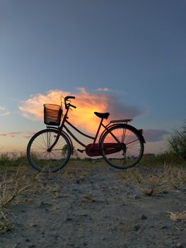 Silhouette of a red bicycle against a vibrant dusk sky in Kecamatan Sukodono, Indonesia.