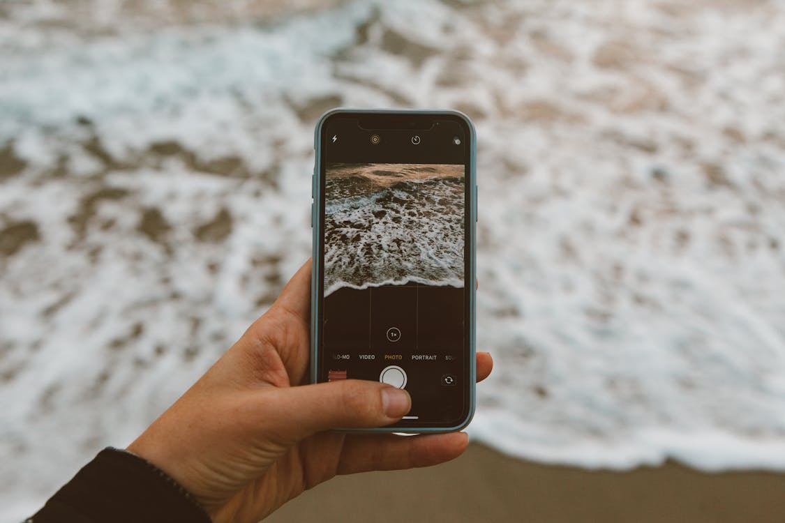 A person holding a phone, taking a picture of the waves