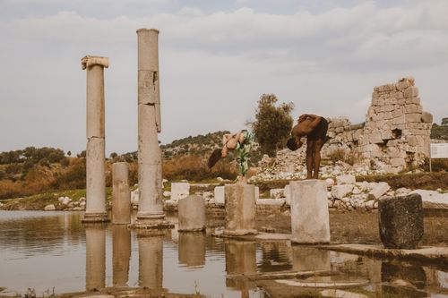 Free Two adults stretching on stone columns in an ancient ruin setting, promoting fitness. Stock Photo