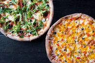 Overhead view of delicious pizzas with mushroom and pepperoni pieces under fresh herb leaves on dark background