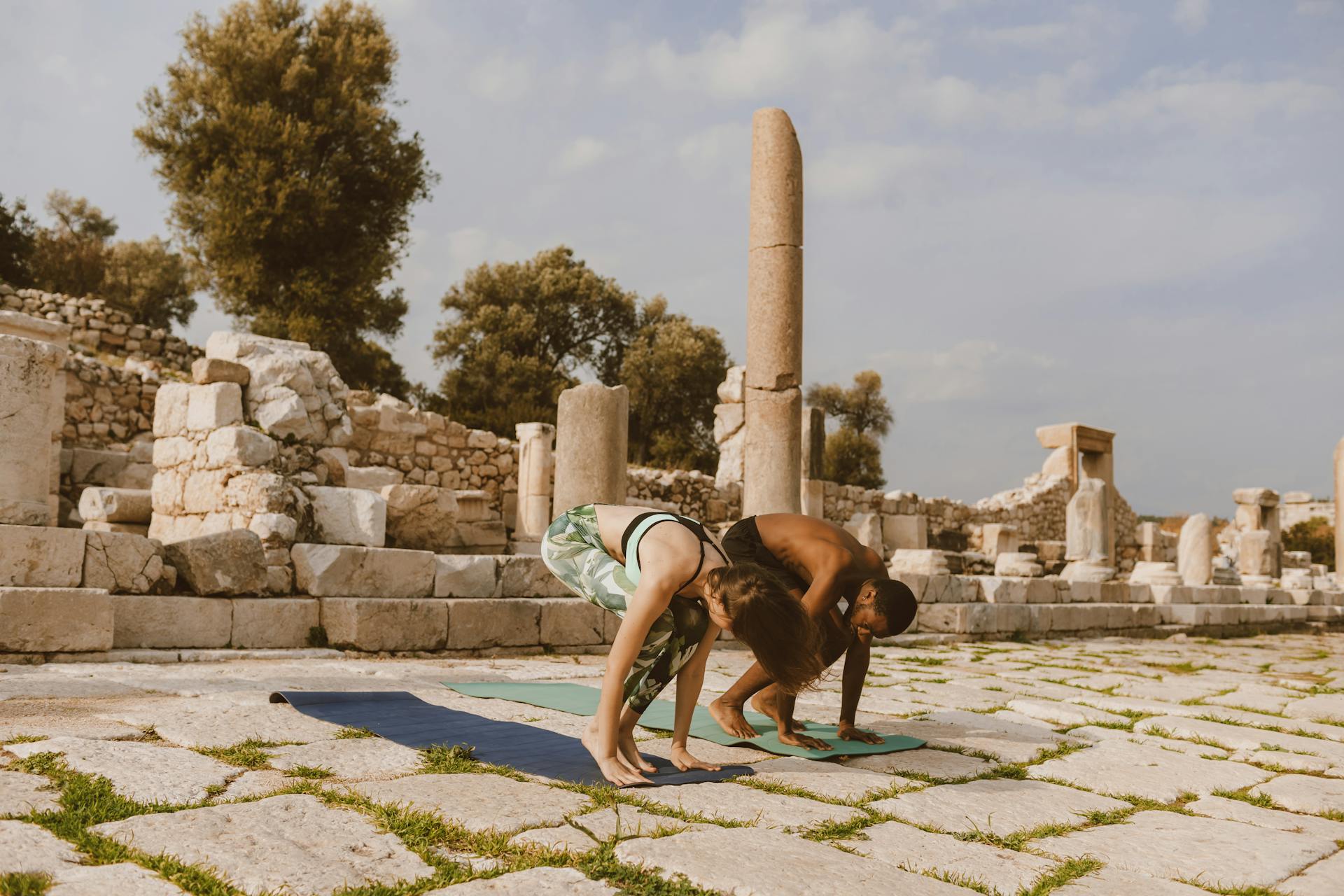 A man and woman perform yoga in a serene ancient ruins setting.