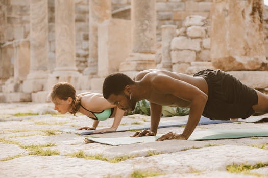 A man and woman practice yoga poses on mats amidst ancient ruins outdoors.