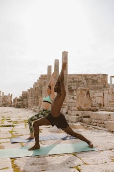 Two people practicing yoga outdoors, surrounded by ancient ruins.