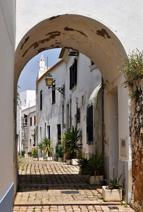 Free Narrow cobblestone street in Albufeira, Portugal, framed by an old arch, capturing rustic charm. Stock Photo