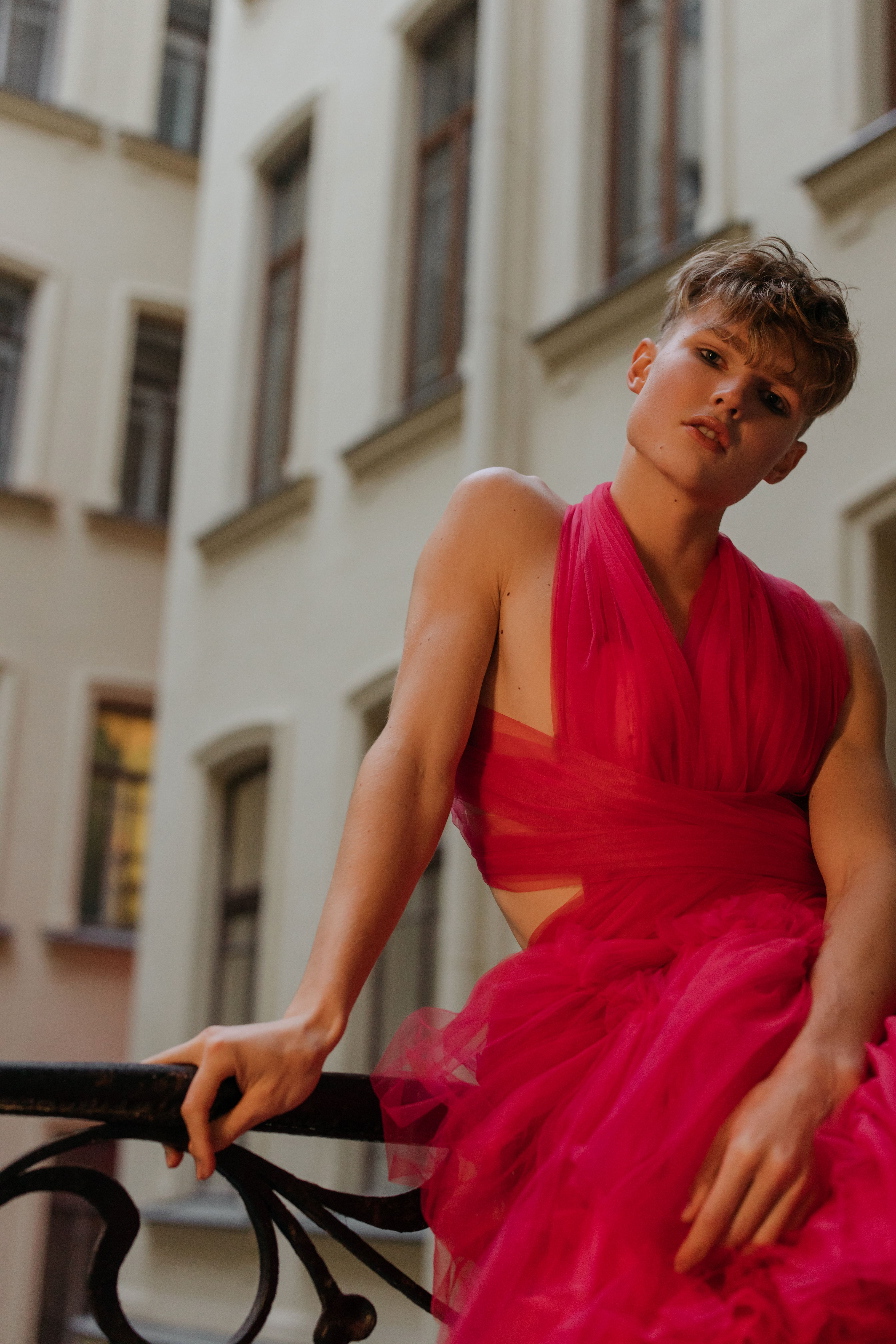 Trendy model in a vibrant pink gown poses outside a classic building, exuding elegance.