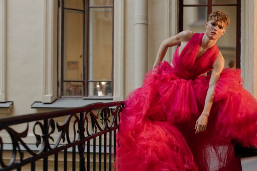 A stylish individual posing elegantly in a vibrant red gown indoors.