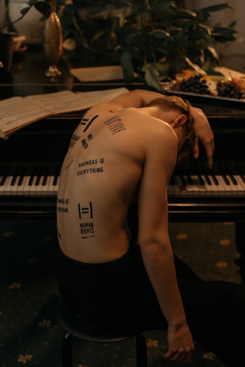 A Shirtless Man Sitting in Front of the Piano