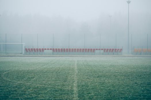Foggy soccer field with empty bleachers, creating a serene and mysterious atmosphere.