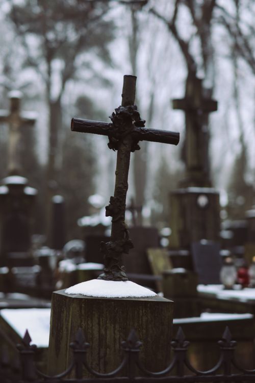 Free A somber view of a snow-covered cross in a quiet winter cemetery setting. Stock Photo
