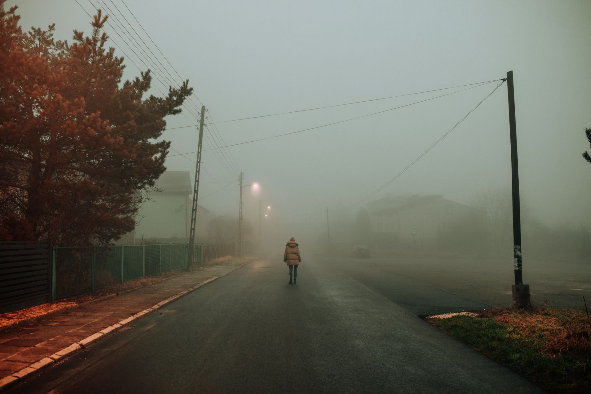 A lone person walks on a foggy, dimly lit street, creating a moody atmosphere.