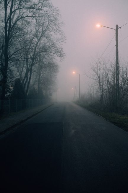 A quiet, foggy street with dimly lit street lamps at night, creating a moody and mysterious atmosphere.