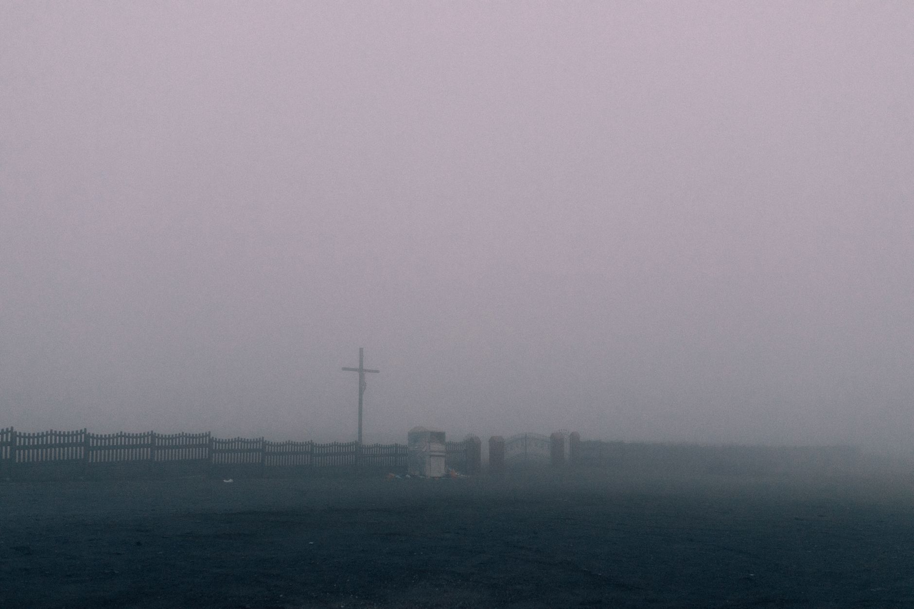 A foggy cemetery with a cross and graves shrouded in mist, creating a somber atmosphere.