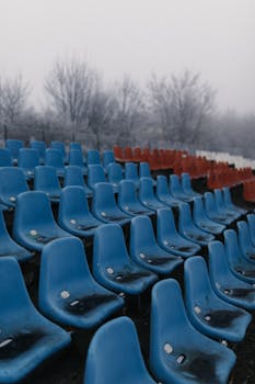Rows of weathered blue and red plastic seats in an empty outdoor sports ground during winter.