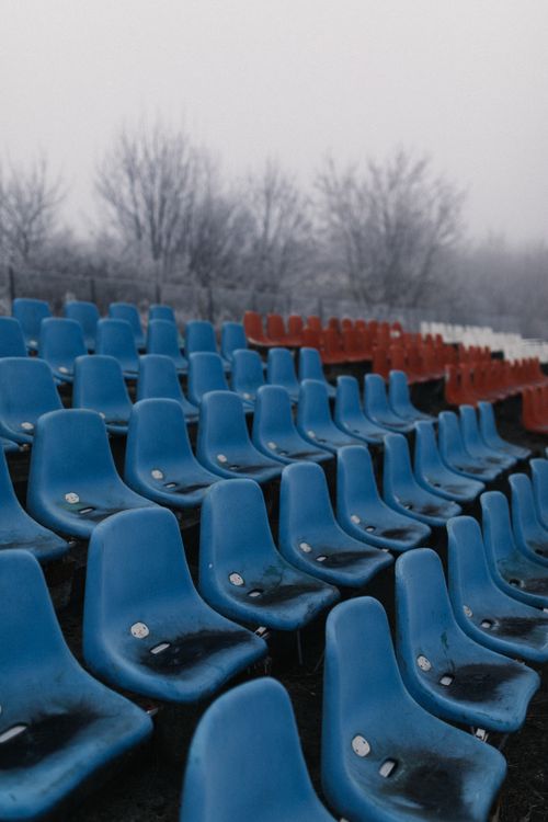 Free Rows of weathered blue and red plastic seats in an empty outdoor sports ground during winter. Stock Photo