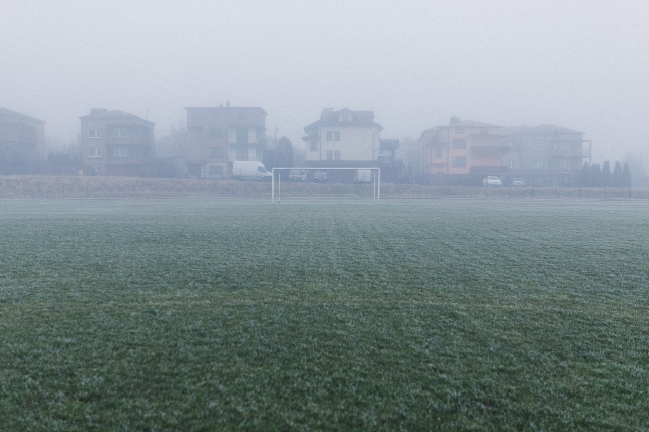 a foggy soccer field with houses in the background creates a serene wi