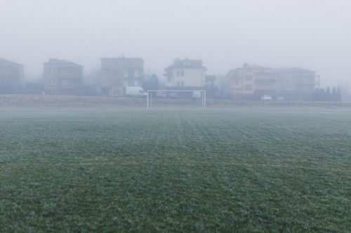 Free A foggy soccer field with houses in the background creates a serene winter morning scene. Stock Photo