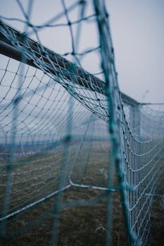 Close-up of a football goal net outdoors on a gloomy day, captures the misty atmosphere.