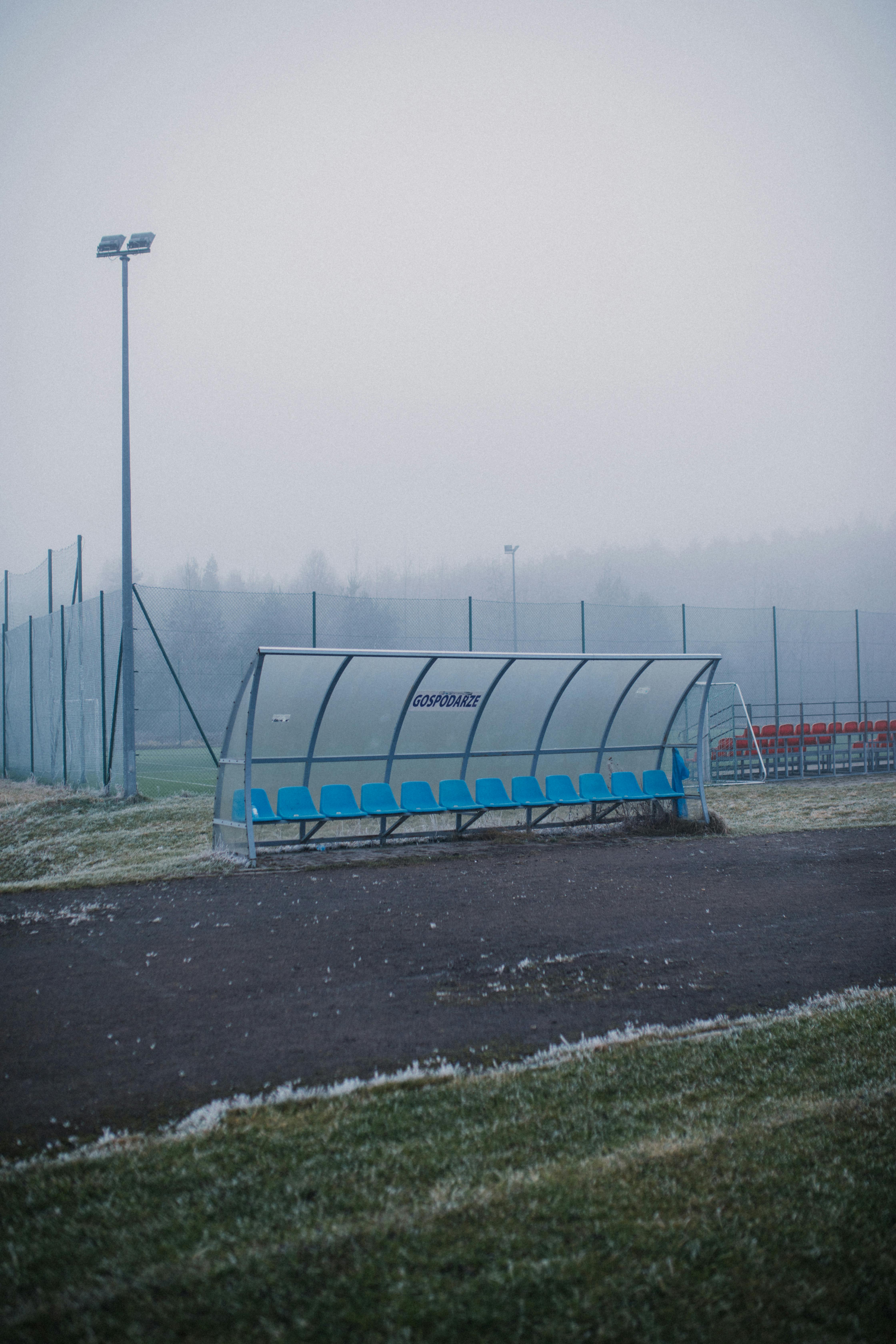 Empty blue seats under a canopy on a fog-covered sports field.