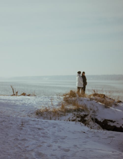 Two People Standing on the Bank of the River in Winter 