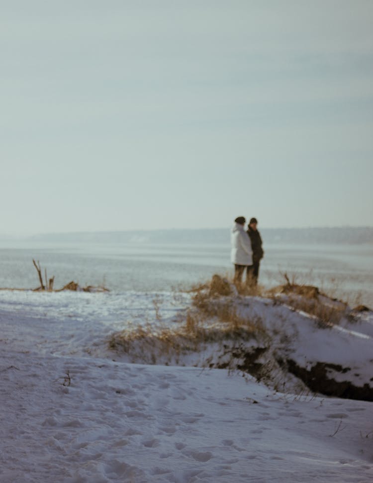 Two People Standing On The Bank Of The River In Winter 