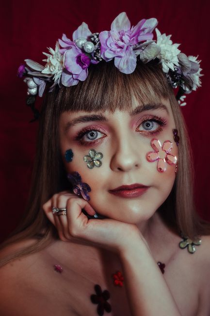 Portrait of a woman with floral wreath and creative makeup featuring flower designs.