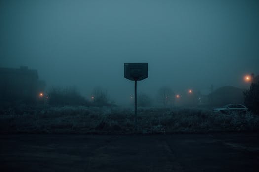 A foggy basketball court in a dimly lit, gloomy atmosphere during twilight.