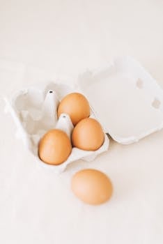 Brown eggs in an open carton against a soft background, highlighting simplicity and freshness.