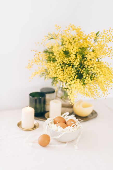 Elegant Easter table setup with yellow mimosa flowers, candles, and brown eggs.