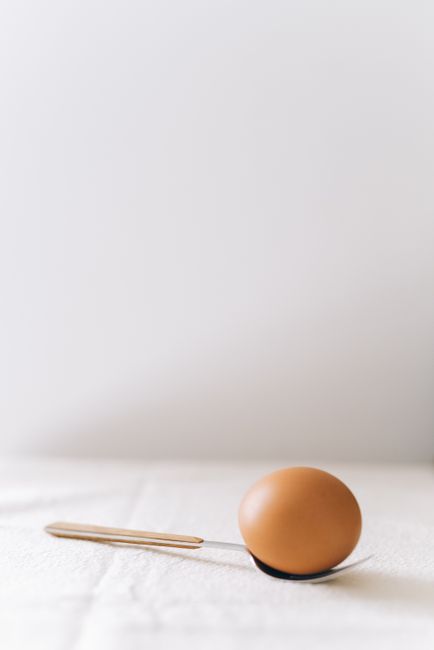 A simple and elegant still life of a brown egg resting on a spoon against a neutral background.