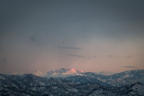 From above spectacular landscape of rough rocky mountain range covered with snow in sunlight at sunset time with cloudy sky