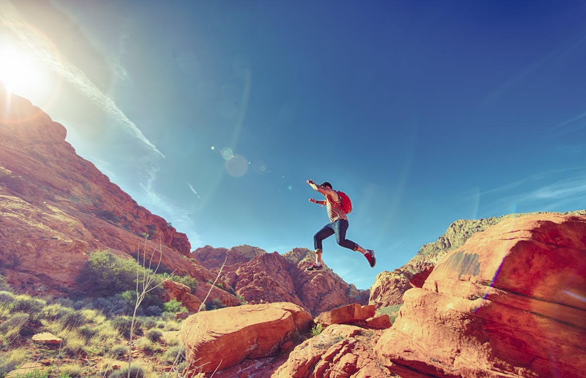 Free Man Jumping on Rock Formation Under Blue Sky Stock Photo