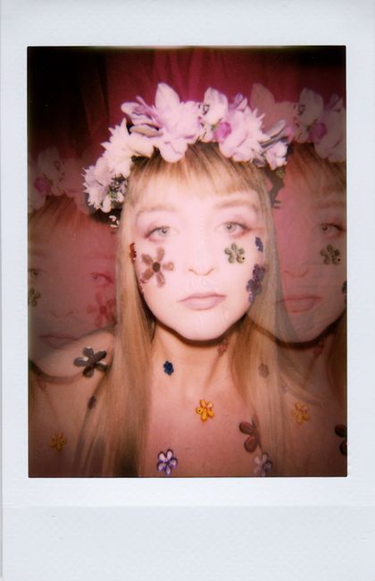 Creative portrait of a woman with a floral crown and petal decorations under warm lighting.