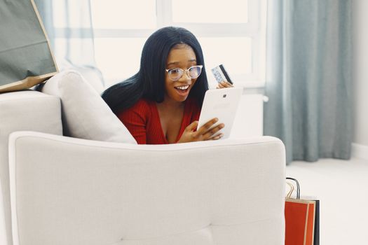 A joyful woman holding a credit card and tablet, shopping online from her sofa.