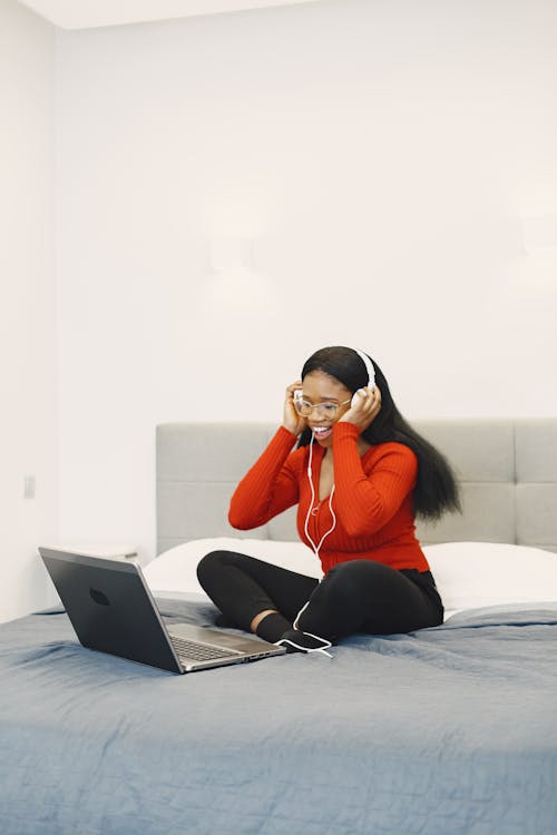 Smiling Woman Using Laptop and Headphones on a Bed 
