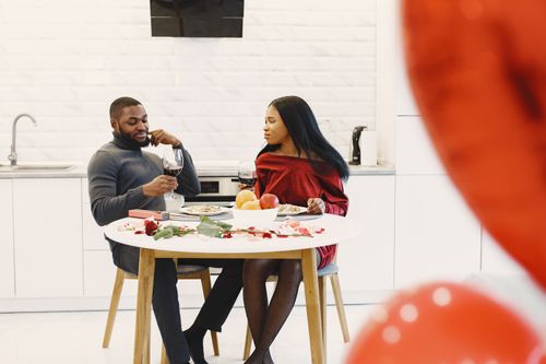 Free A couple enjoying a romantic dinner at home with wine, roses, and fruit on the table. Stock Photo