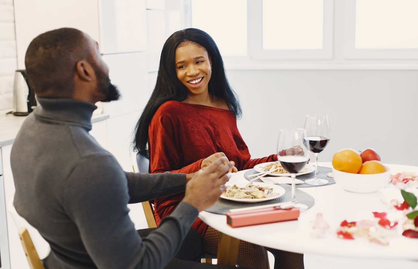 A happy couple enjoys a romantic dinner with wine indoors, surrounded by roses.