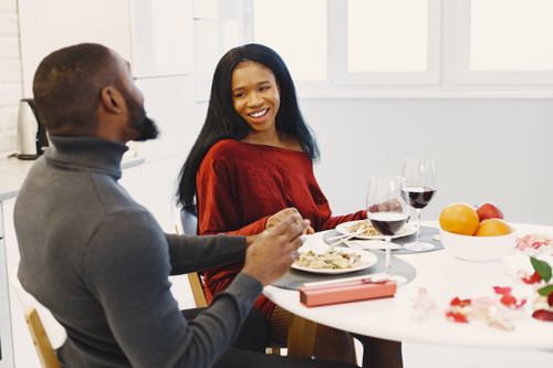 Free A happy couple enjoys a romantic dinner with wine indoors, surrounded by roses. Stock Photo