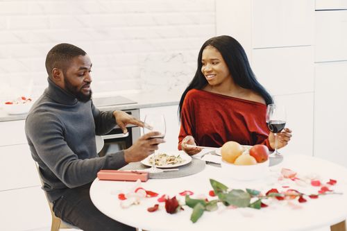 Free A couple enjoys a romantic dinner with wine and roses in a cozy setting. Stock Photo