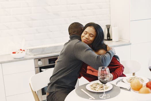 A couple sharing a warm embrace over a romantic dinner in a modern kitchen.