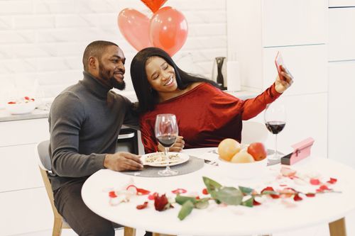Free Couple enjoying a romantic dinner with red wine and balloons, taking a selfie for a special occasion. Stock Photo