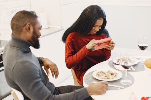 Free Happy couple enjoying a romantic dinner, exchanging gifts and savoring wine at home. Stock Photo