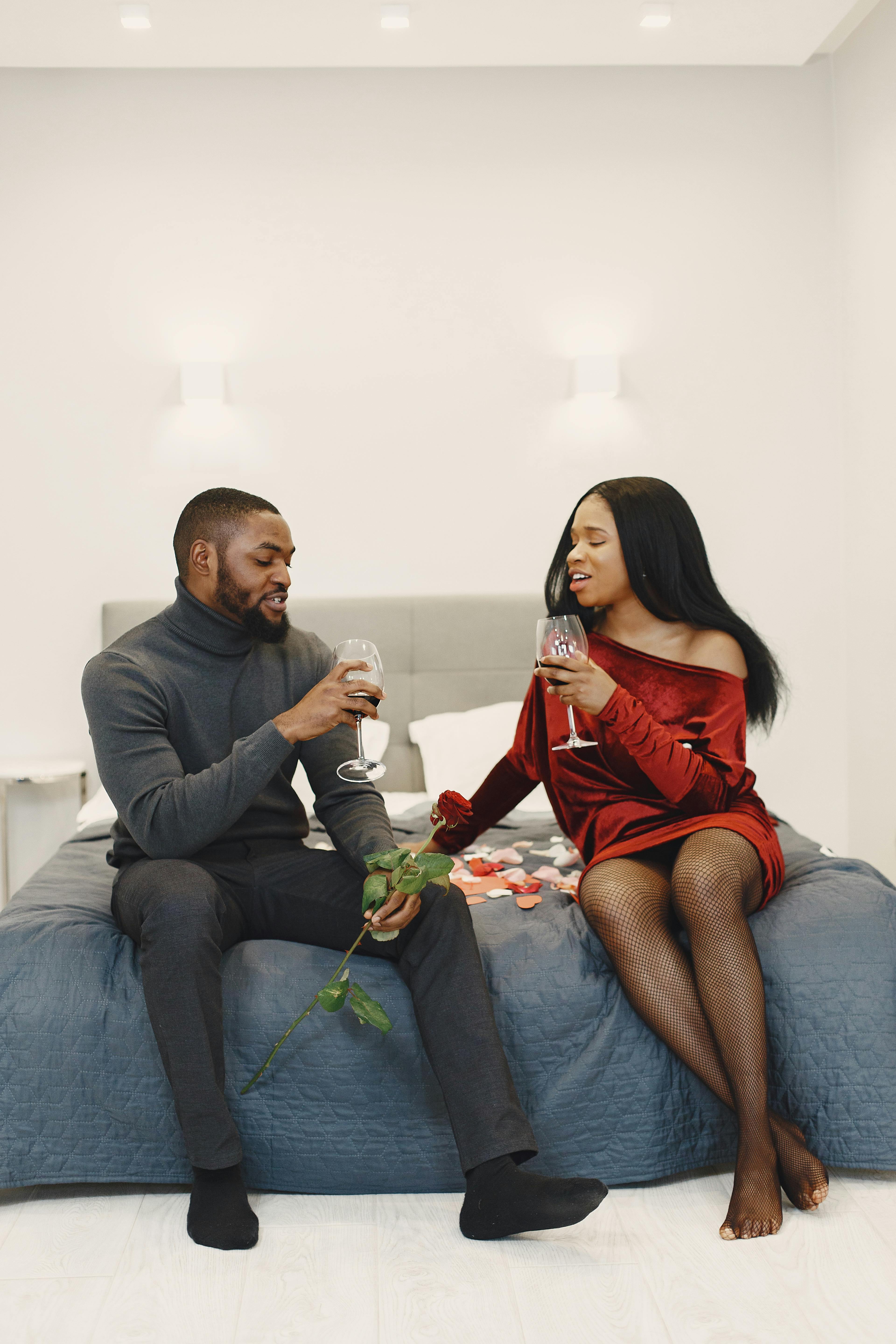 Couple sharing a romantic moment with wine and roses in a cozy bedroom setting.