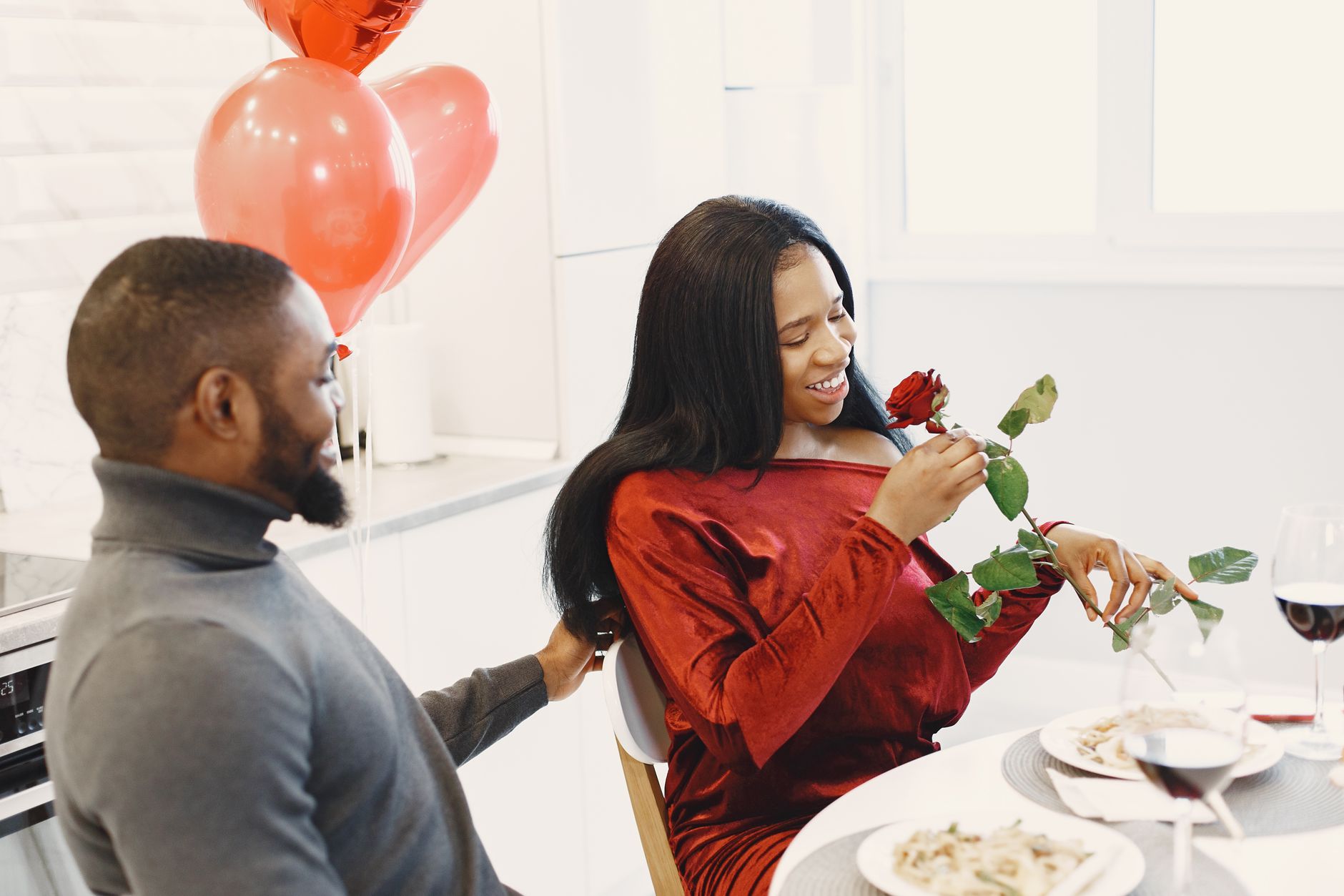 Happy couple enjoying a romantic dinner with red wine and roses, perfect for Valentine's celebration.