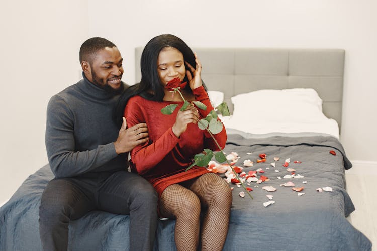 Romantic Couple Sitting On A Bed Covered With Rose Petals 