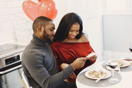 Free Couple enjoying a romantic dinner indoors with balloons and smiles. Stock Photo