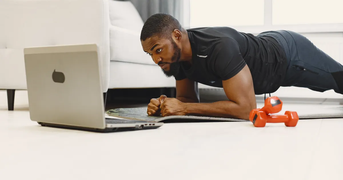 Someone holding a plank at home next to an open laptop