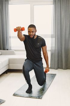 African American man doing a lunge with dumbbells in a living room setting, focused on exercise.
