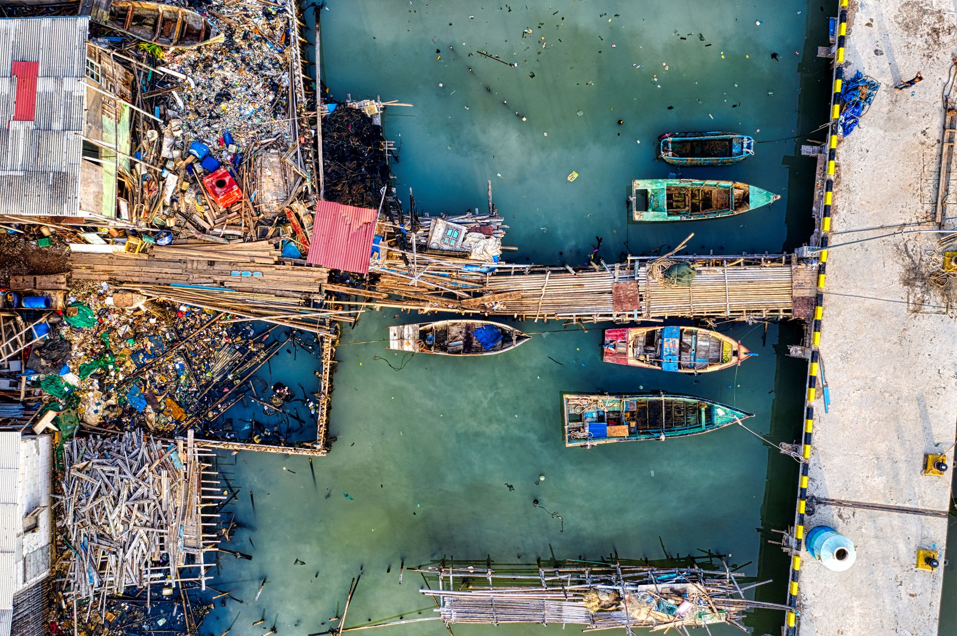 A striking aerial view of a polluted canal in Jakarta, showing boats amidst debris and garbage.