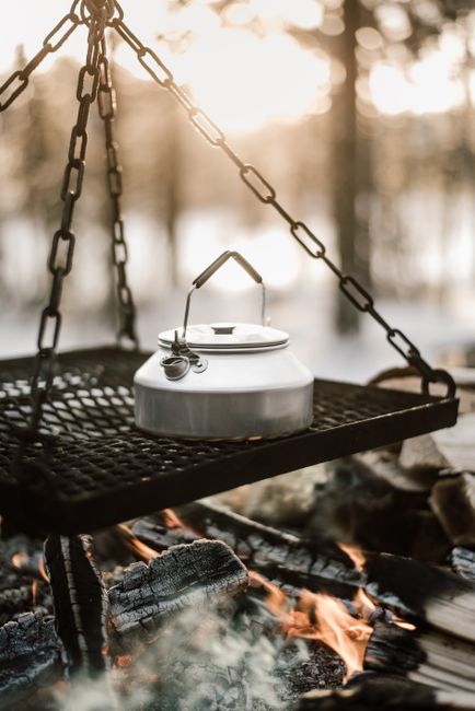 Rustic campfire scene with a kettle hanging over a burning fire, perfect for outdoor cooking concepts.